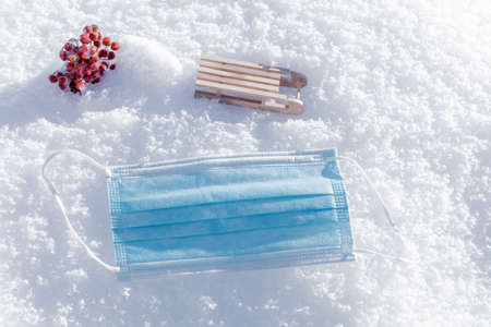 Medical mask and decorative wooden sleds in the snow. Health concept, protect yourself on winter...