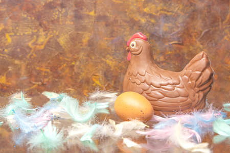 Chocolate chicken and egg, multi-colored feathers on a brown background. Concept, Easter, congratulation, levitation, There is a place for text. High quality photoの写真素材