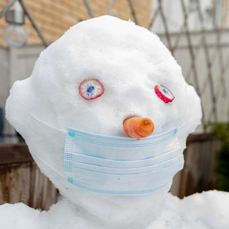 In the courtyard of the house there is a snowman in a medical mask. Concept, spring, protect...