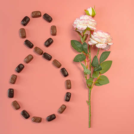 Rose flower lined with candies with number 8. Layout on pink background. Greeting card with spring...