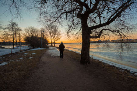 Dawn in the spring by the sea. A man walks along the alley on the embankment in Helsinki, Finland