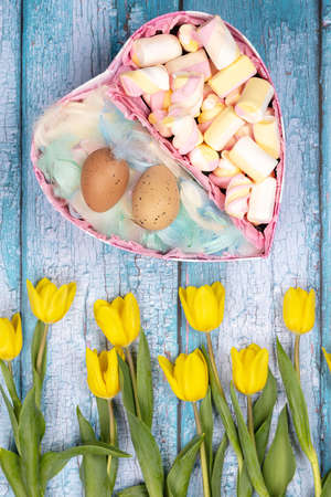 Spring composition of yellow flowers, a tulip, a basket of sweets and eggs on a blue background....