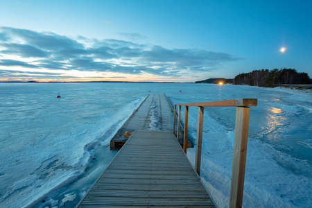 Winter sunrise over a lake covered with ice. Moon in the blue sky. Finland, Scandinavian natureの写真素材