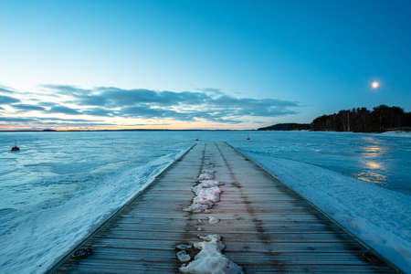 Winter sunrise over a lake covered with ice. Moon in the blue sky. Finland, Scandinavian natureの写真素材