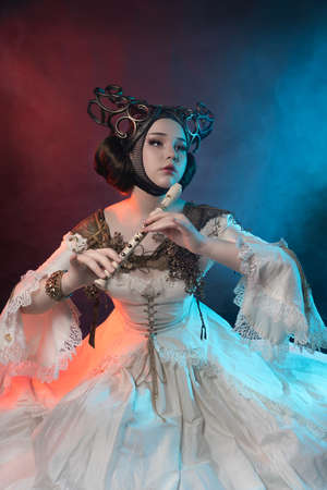 A mythical creature, a beautiful girl in a white, fairy-tale costume with a pipe in her hands. Photo...
