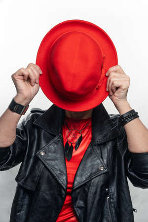 Elegant woman at the age, in a red hat and a red sweater older model posing in studio. Youth in...