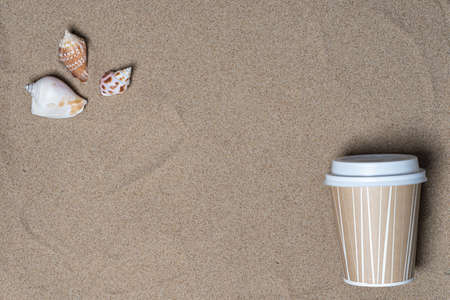 Seashells and a cup for coffee on the sand, top view, there is a place for text. Summer vacation concept by the seaの写真素材