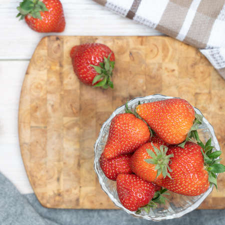 The strawberries lie in a glass vase with a row of scattered berries. ... On a wooden stand, layout, top view. Summer concept, harvestingの写真素材