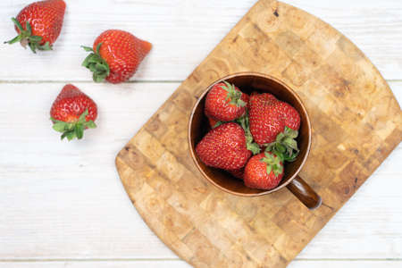 Strawberries lie in a wooden mug with a row of scattered berries. ... On a wooden stand, layout, top view. Summer concept, harvestingの写真素材