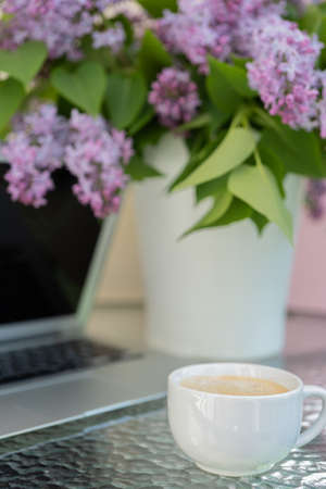 On the table are a bouquet of lilacs and a computer, a cup of coffee. Concept, work at home.の写真素材