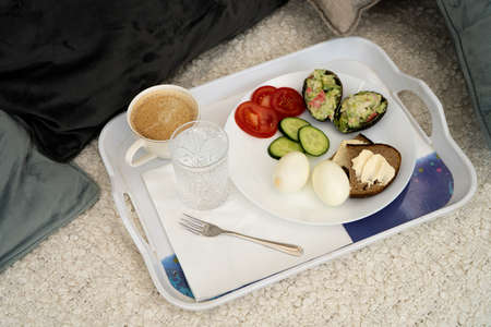 Breakfast on the bed Vegetables tomatoes and cucumbers salad of avocado and eggs. Serving white...