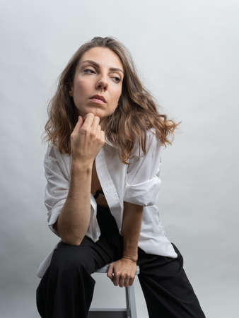 Model, brunette posing on a white background in the studio. She is wearing a white shirt, a black hairstyle. Photo to the waistの写真素材