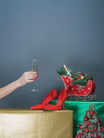 Hand with a glass of shompansky and beautifully wrapped gifts and Christmas tree decorations on a gray background. There is room for text. The concept of gifts, congratulations for Christmas, for the New Yearの写真素材