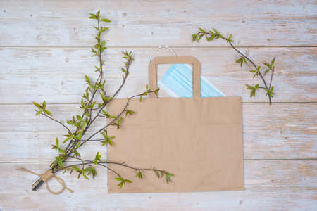 Medical, protective face mask, a bouquet of green willow twigs, a paper bag on a wooden background. There is room for text. Protected from covid for shoppingの写真素材