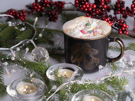 A mug of coffee, sprigs of spruce, New Year's garland, a candle on the table. Christmas decorations,...