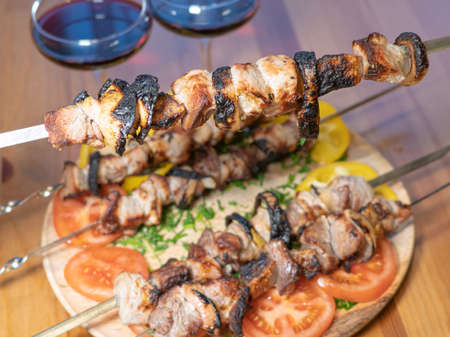 meat on skewers, pieces of fried pork, barbecue. Dish with vegetables and glasses with red wineの写真素材