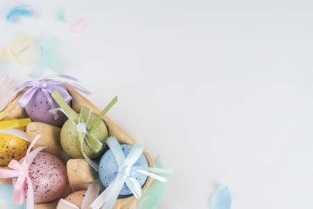 Easter colored eggs in a box, on a white background decorated with colored feathers. There is space for text. View from aboveの写真素材