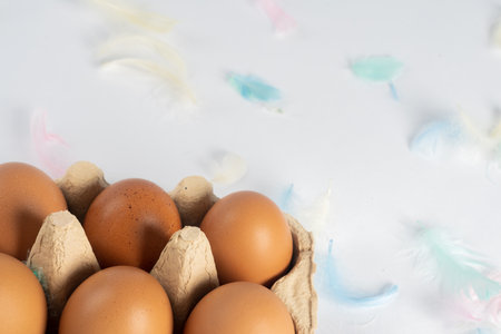 brown eggs in a box, on a white background, decorated with colored feathers. There is space for text. Top view Easter conceptの写真素材