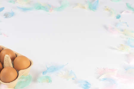 brown eggs in a box, on a white background, decorated with colored feathers. There is space for...