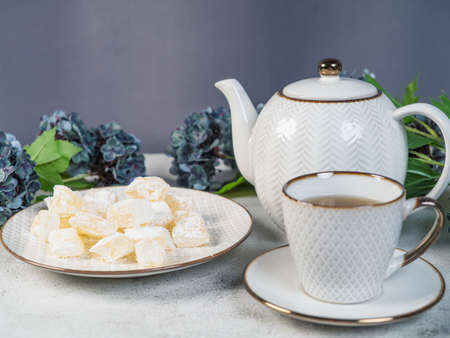 A teapot and a white mug on the table, flowers and traditional Turkish and Greek jelly candies in...