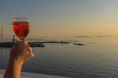 A glass of red wine in hand against the backdrop of a sunset on the sea. Sunny, summer evening. sea cruise. There is space for text. Peace, love conceptの写真素材