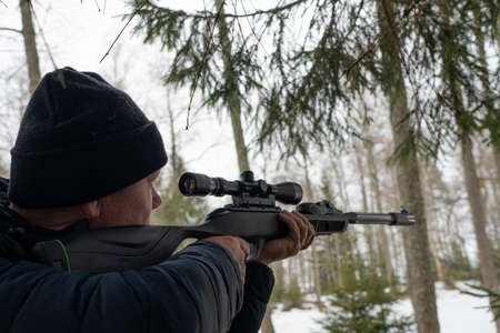 A man with a rifle in the spring forest, the hunter holds a rifle and waits for prey, the hunter shootsの写真素材