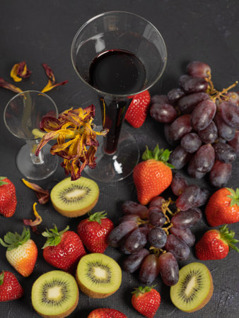 Strawberries and grapes, kiwi, a glass of wine. Top view.on a black background. Vase with old flowers .Concept dissert, vitaminsの写真素材