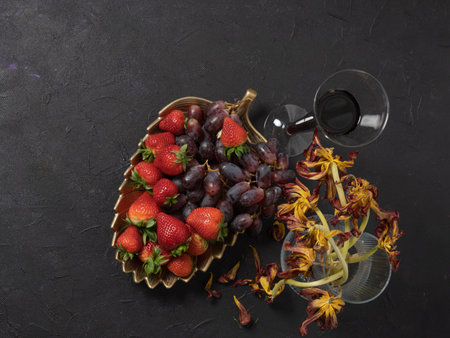 Strawberries and grapes, kiwi, a glass of wine. Top view.on a black background. Vase with old flowers .Concept dissert, vitaminsの写真素材