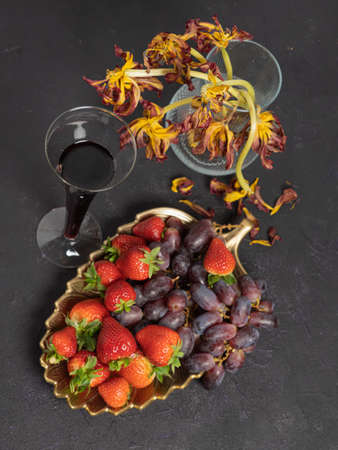 Strawberries and grapes, kiwi, a glass of wine. Top view.on a black background. Vase with old flowers .Concept dissert, vitaminsの写真素材