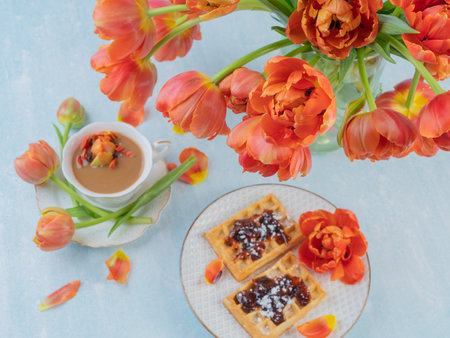 Scarlet, red tulips in a vase and a white cup with coffee and French waffles. The concept of congratulations and old holidays. There is a place for text.の写真素材