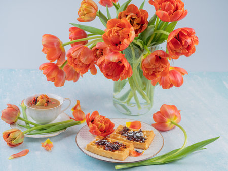 Scarlet, red tulips in a vase and a white cup with coffee and French waffles. The concept of congratulations and old holidays. There is a place for text.の写真素材