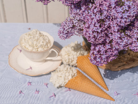 A bouquet of lilacs in a basket and a tea set. Ice cream waffle cones are decorated with flowers. close-up topの写真素材