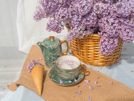 A bouquet of lilacs in a basket and a tea set. Ice cream waffle cones are decorated with flowers. side view background whiteの写真素材