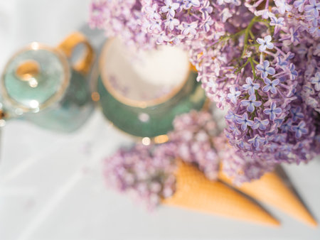 A bouquet of lilacs in a basket and a tea set. Ice cream waffle cones are decorated with flowers. close-up topの写真素材