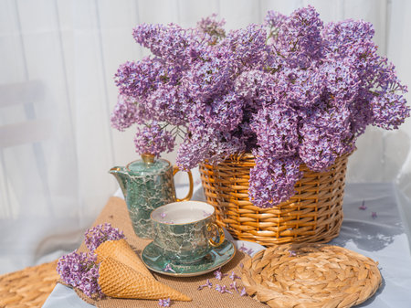A bouquet of lilacs in a basket and a tea set. Ice cream waffle cones are decorated with flowers. side view background whiteの写真素材