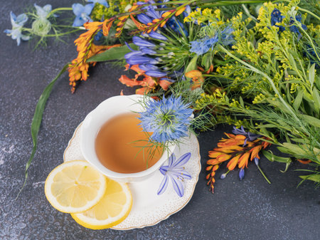 teatime. A bouquet of flowers and a cup of black tea with lemon on a gray background. top view.の写真素材