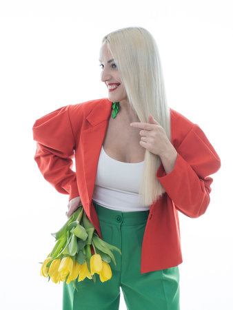 A fashionable snapshot. A beautiful blonde posing in bright clothes on a white background with yellow tulips in her hands. Beauty, fashion concept.の写真素材
