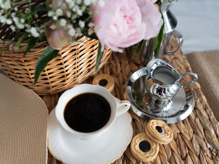 An artistic still life with pink peonies in a wicker basket, a cup of coffee, cream and cookies. top view. horizontal photo.の写真素材