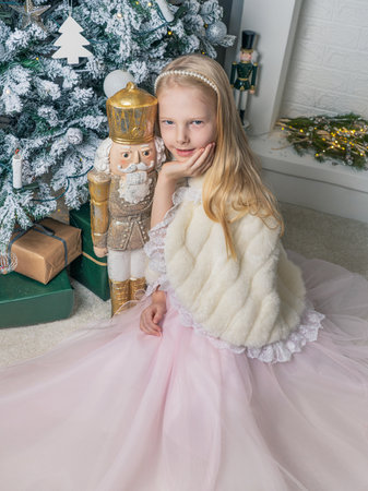 Portrait of a beautiful little girl in a pink dress in the interior with Christmas decorations. A girl poses next to a golden Nutcracker. Magical Christmas time.の写真素材