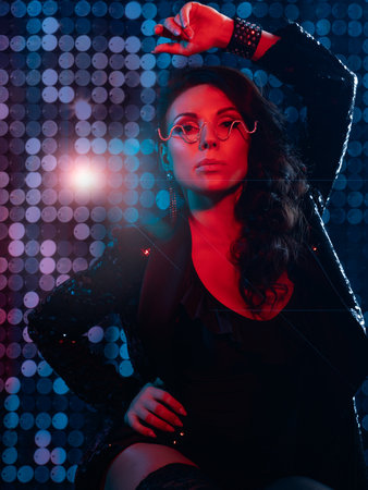 A gorgeous brunette in a black bodysuit, black stockings and a sequined jacket at a party. nightclub. Red backlight in the dark. Photo with colored light.の写真素材