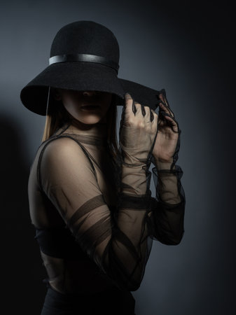 Fashion portrait of a young girl in a black bra and transparent top. Felt black hat. Model posing, faces not visible photo in studio.の写真素材
