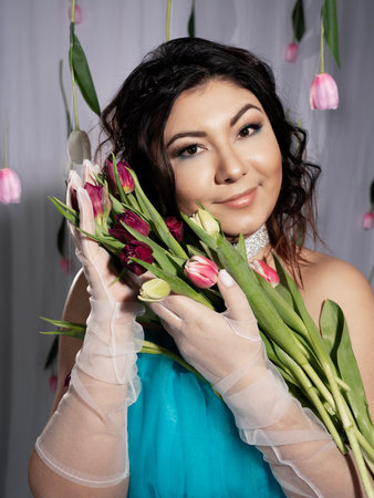 Beautiful, woman in a festive blue dress, close-up portrait, surrounded by natural flowers with a bouquet of tulips. spring photo. March 8の写真素材
