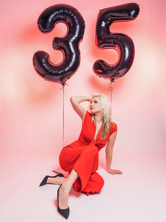 Beautiful blonde in red evening dress and balloons 35 . Celebrates his birthday. pink background.の写真素材