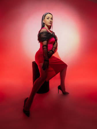 Portrait of a beautiful brunette in a red dress on a pink background. She is wearing elegant black gloves.の写真素材