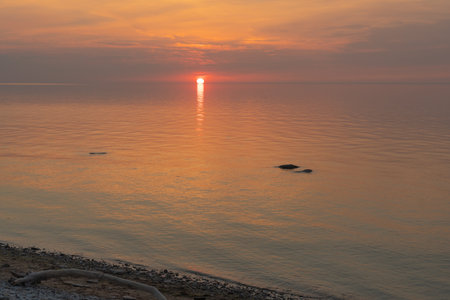 Summer sunset on the shore of the bay in Toila Oru Park. Orange sky. Ripples on the water from the wind. Pebbles on the shore. Natural background. Space for text.の写真素材