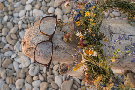 A fancy wooden snag on a pebble beach. Glasses and a wreath of flowers create an image of an unusual creature.の写真素材