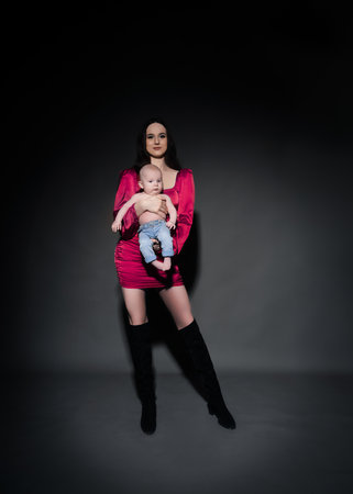 A young, modern, beautiful loving mommy holds hands, kisses her adorable baby in a bodysuit, expresses affection, feels love, close-up. Happy mother's day, motherhood, carefree childhood, guardianship conceptの写真素材