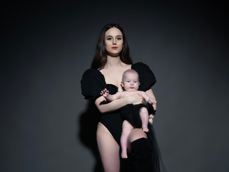A young, modern, beautiful loving mommy holds hands, kisses her adorable baby in a bodysuit, expresses affection, feels love, close-up. Happy mother's day, motherhood, carefree childhood, guardianship conceptの写真素材