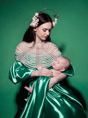 A young, modern, beautiful loving mommy holds hands, kisses her adorable baby in a bodysuit, expresses affection, feels love, close-up. Happy mother's day, motherhood, carefree childhood, guardianship conceptの写真素材