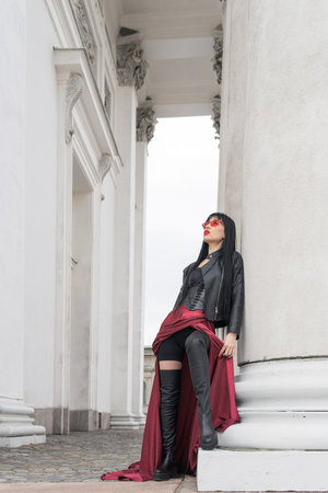 Woman with long hair, perfect figure, sexy. she is in a satin, long red skirt, leather jackets. Posing in the city at the tall ancient columnsの写真素材